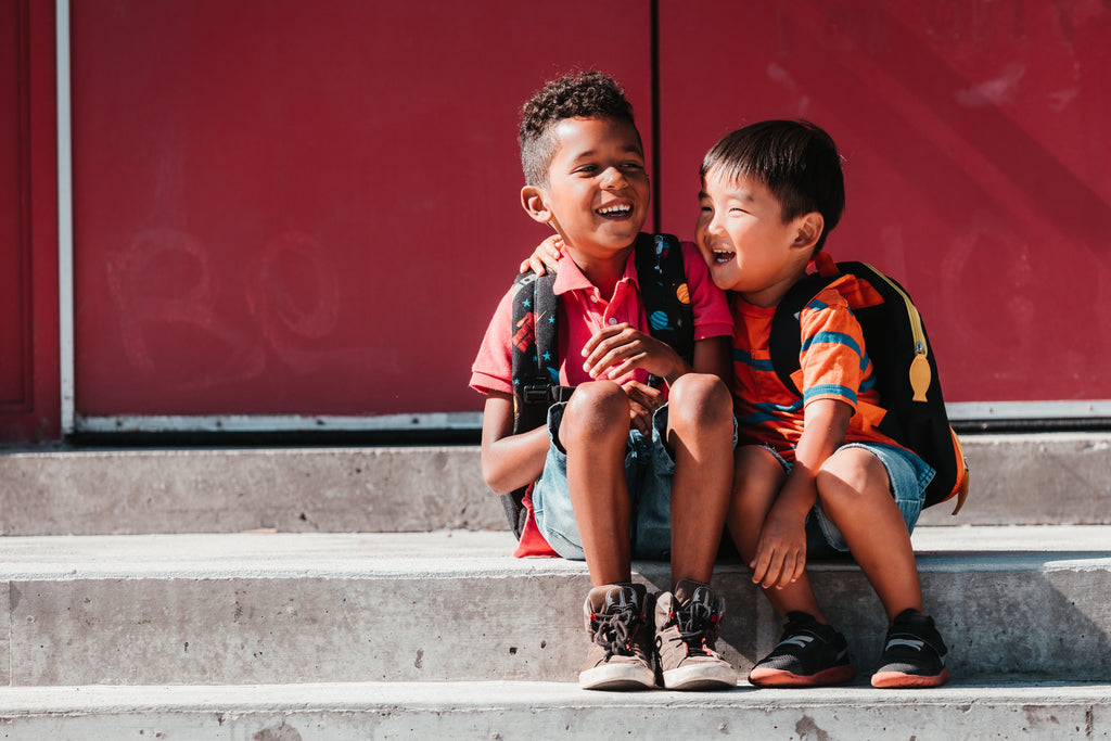 Two elementary school aged boys laughing while sitting on stairs outside of school.