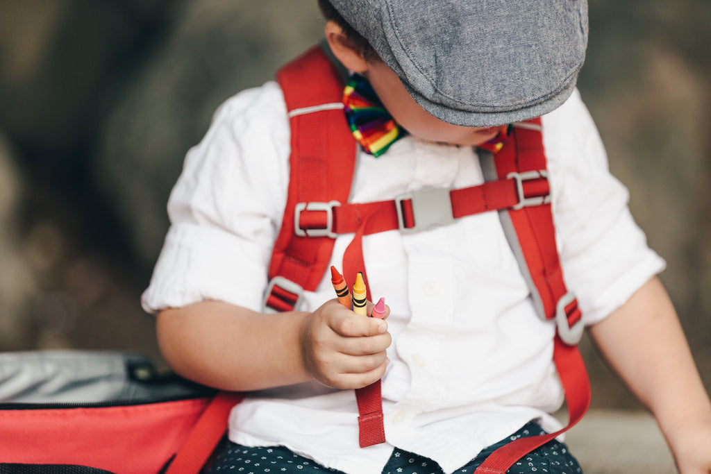 Close up image of a child wearing a red backpack and holding crayons.