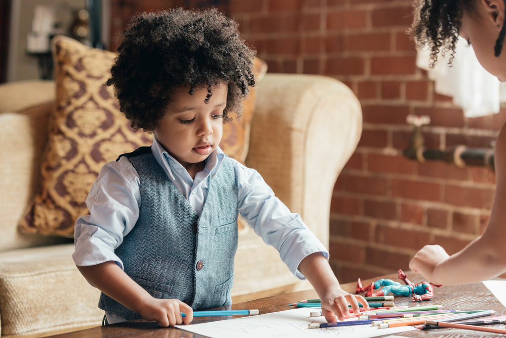 Preschool or kindergarten aged children coloring on white paper on living room table.